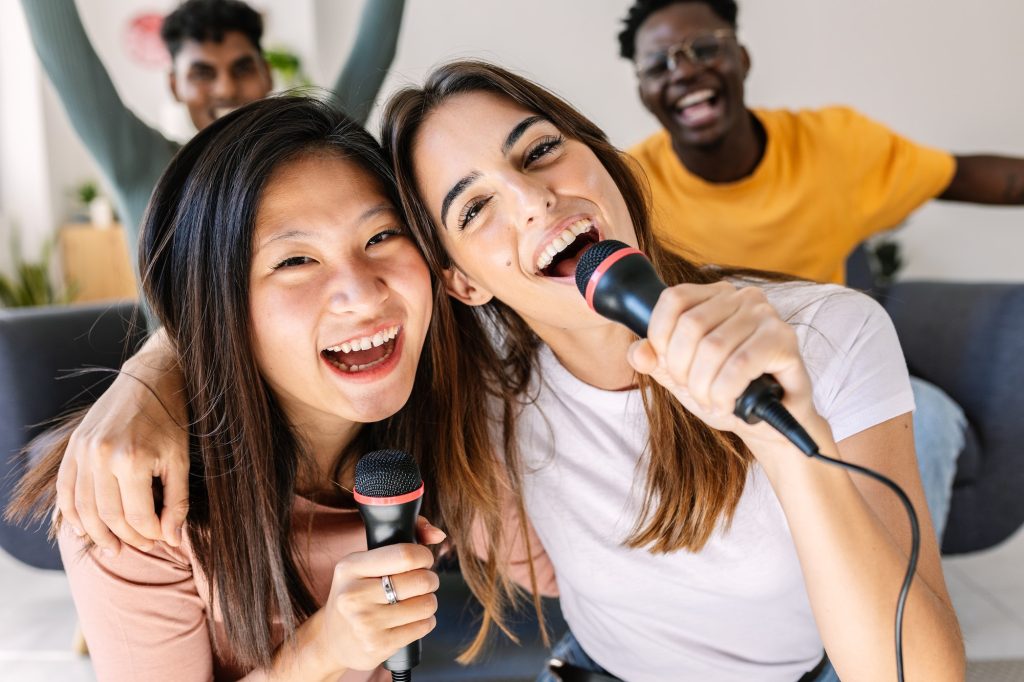 Multiracial young women having fun with friends playing karaoke at home party